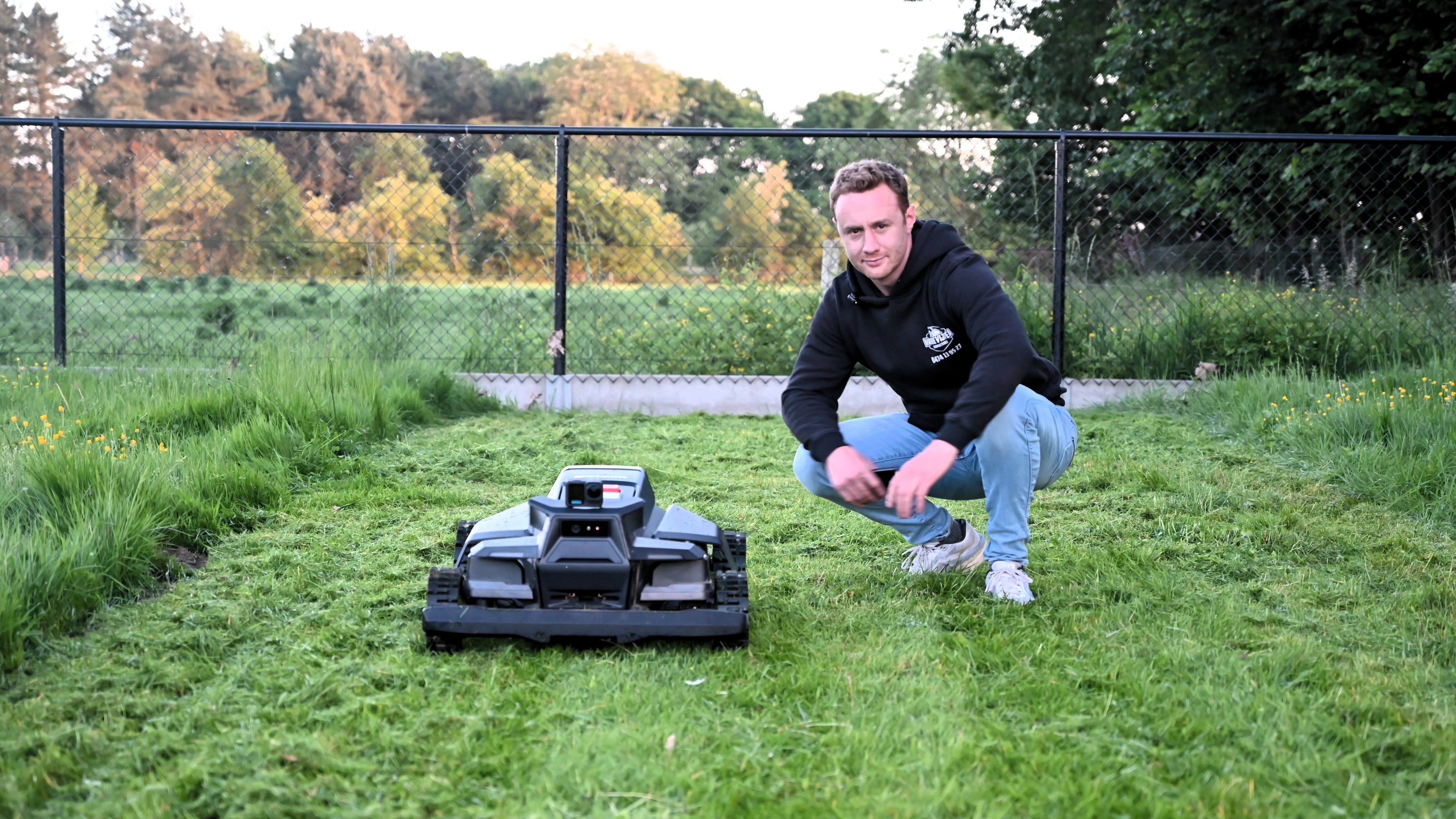 Man kneeling on grass next to a robot lawn mower