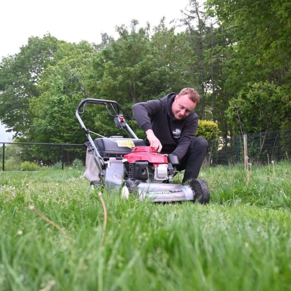 Man operating a lawn mower in a grassy area with trees in the background