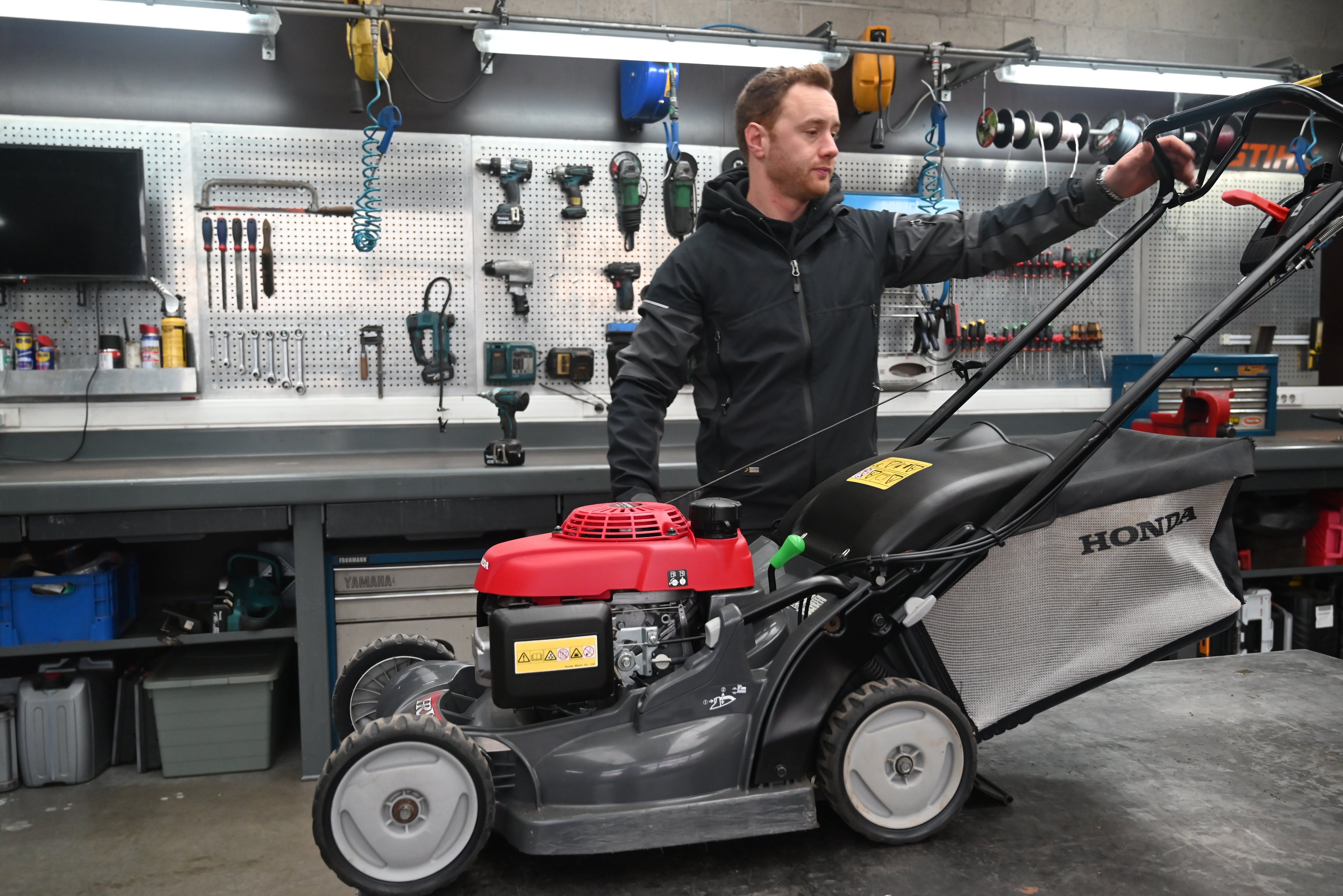 Man inspecting a Honda lawn mower in a workshop.