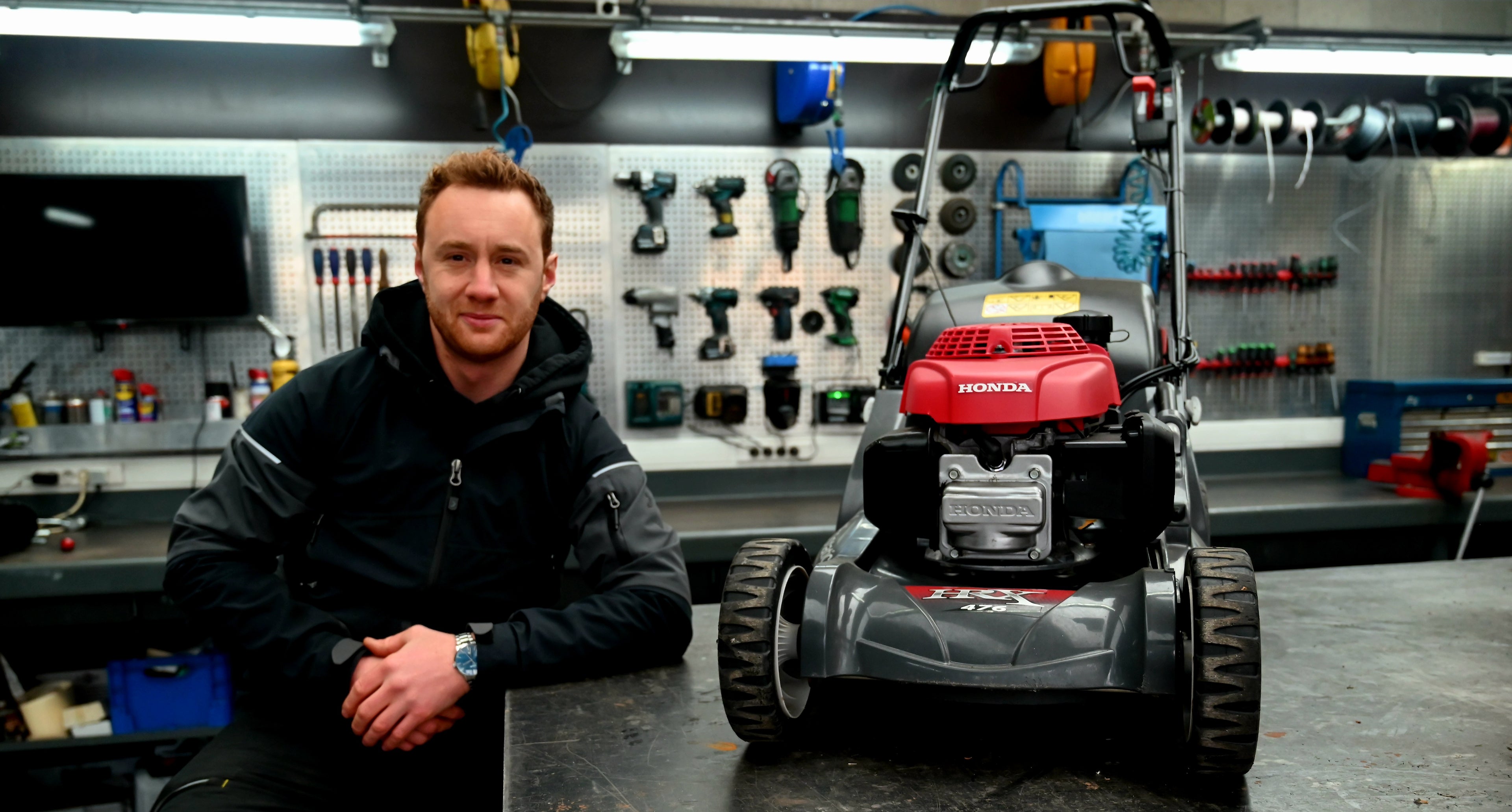Man standing next to a Honda lawn mower in a workshop setting