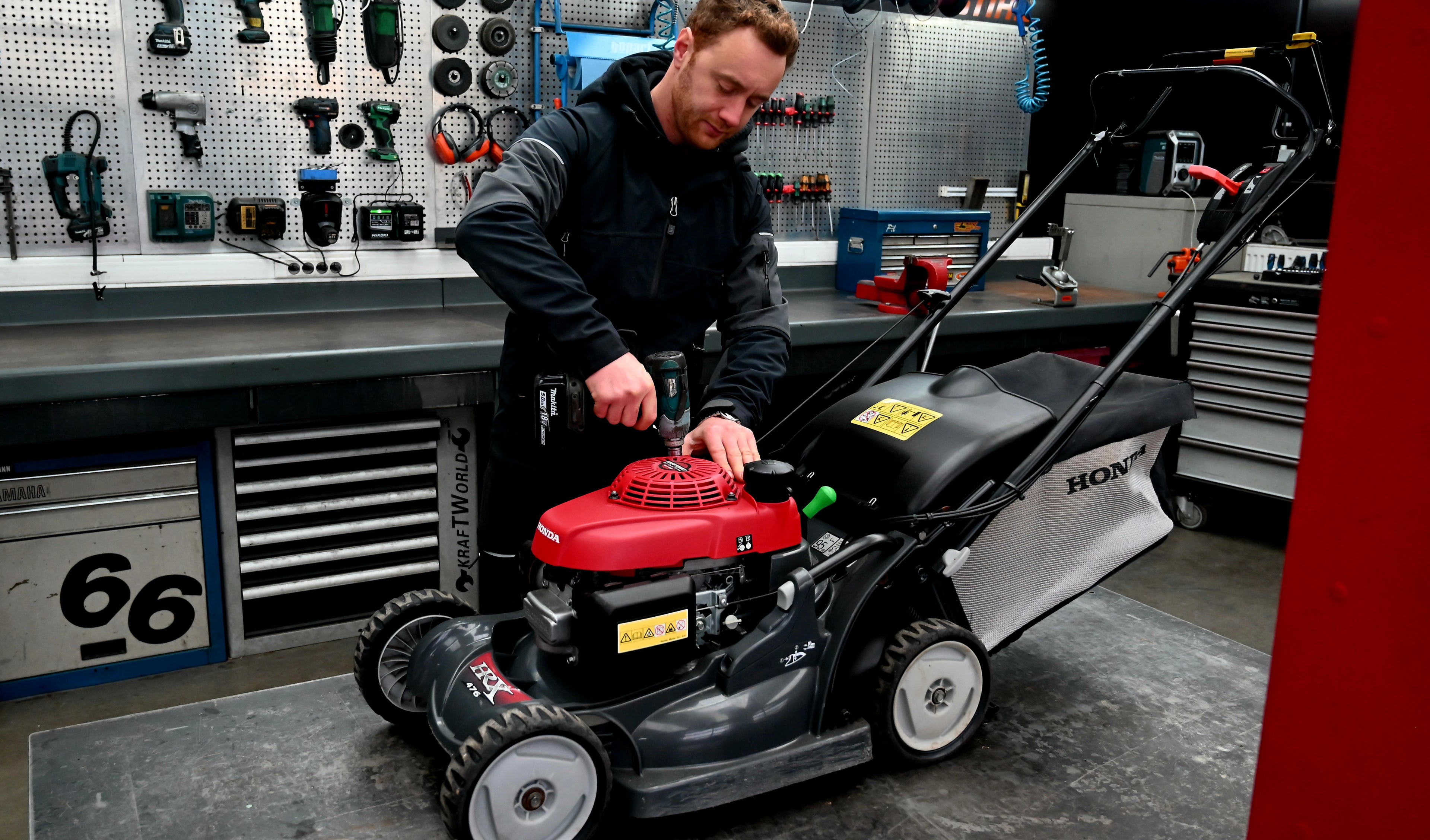 Man working on a Honda lawn mower in a workshop.