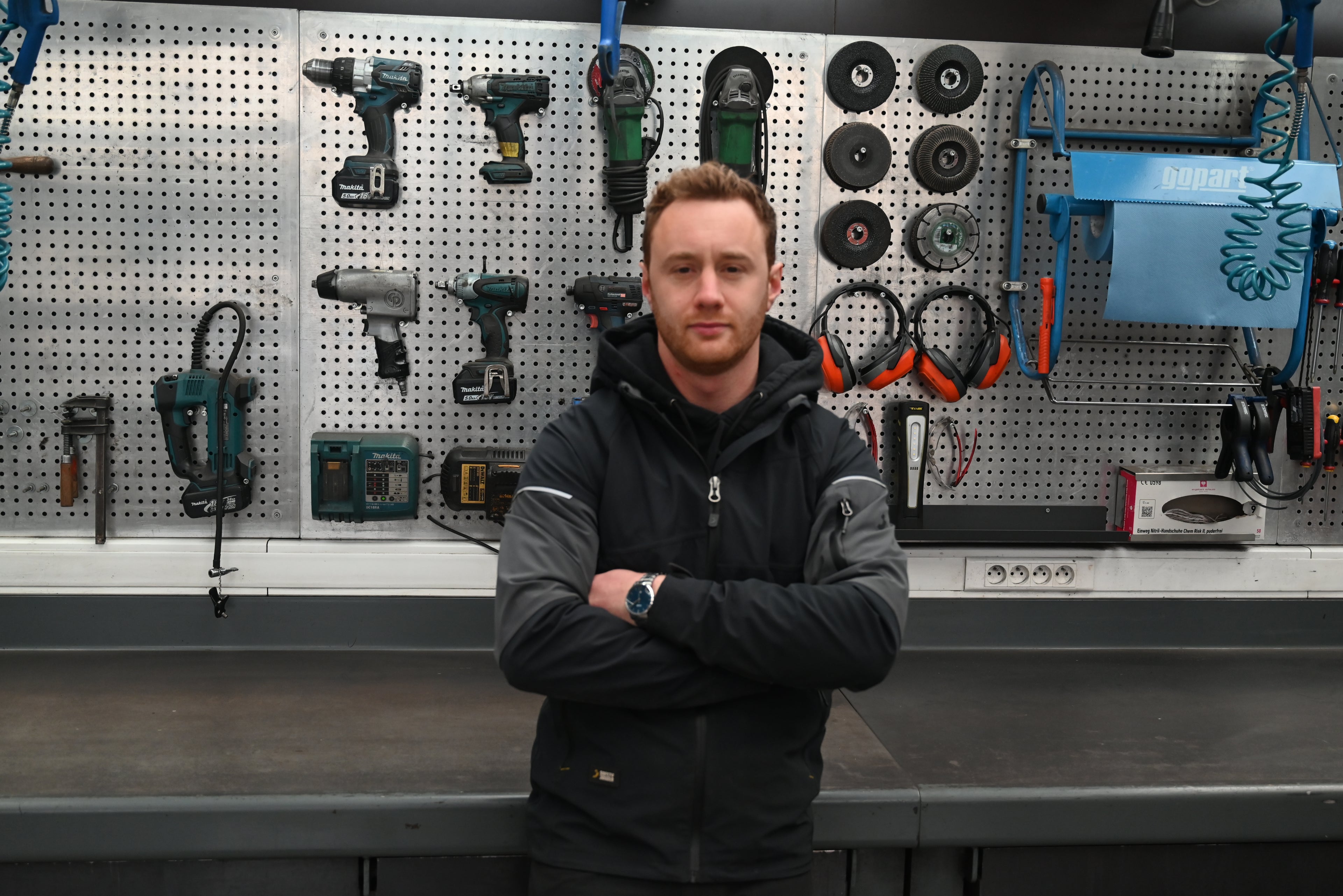 Man standing in a workshop with tools on a pegboard behind him