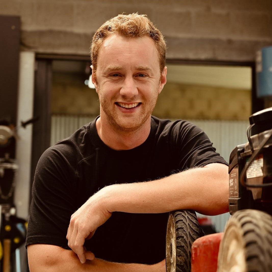 Man in a black shirt leaning against a vehicle in an industrial setting